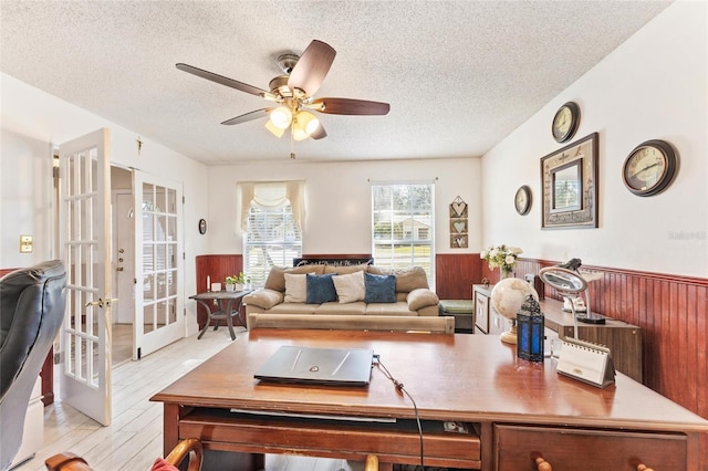 living room with light hardwood / wood-style floors, french doors, a textured ceiling, and wood walls