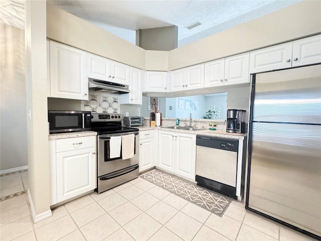 kitchen with sink, light tile patterned floors, appliances with stainless steel finishes, white cabinetry, and a textured ceiling