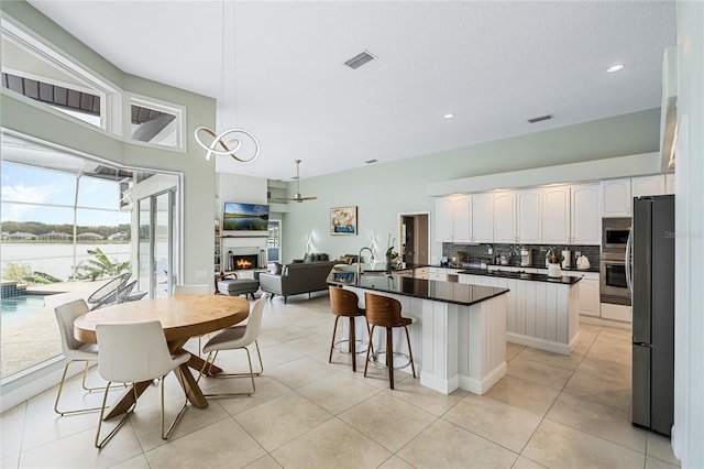 kitchen with appliances with stainless steel finishes, a kitchen breakfast bar, decorative backsplash, light tile patterned floors, and white cabinetry