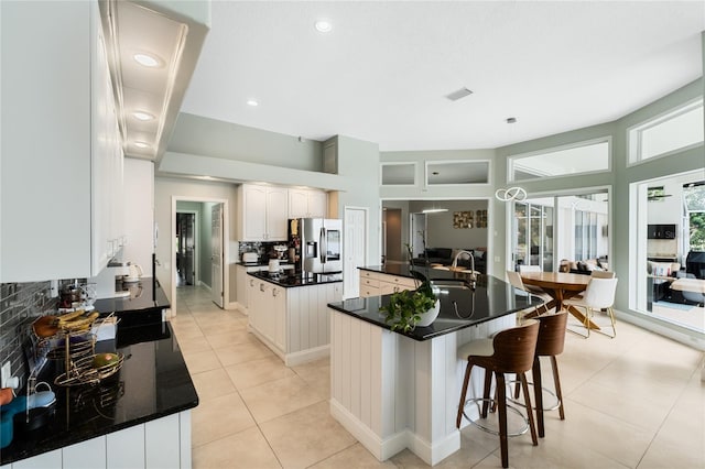 kitchen featuring sink, stainless steel refrigerator with ice dispenser, white cabinetry, an island with sink, and decorative backsplash