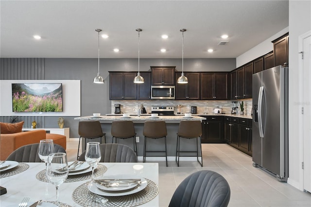 kitchen featuring a breakfast bar, pendant lighting, tasteful backsplash, a kitchen island with sink, and stainless steel appliances