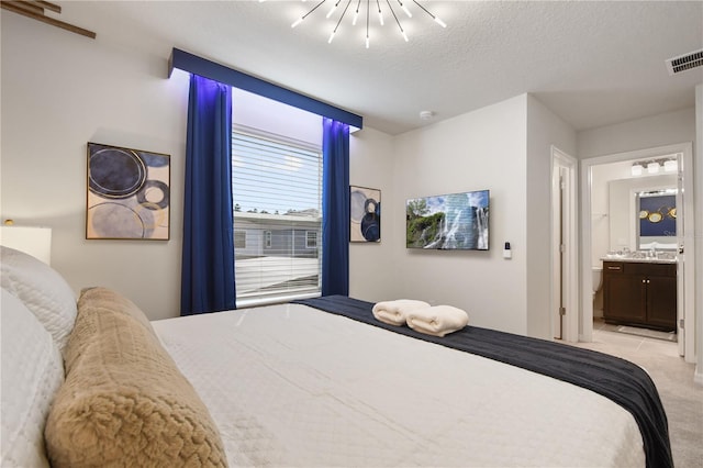 bedroom with ensuite bath, light carpet, and a textured ceiling