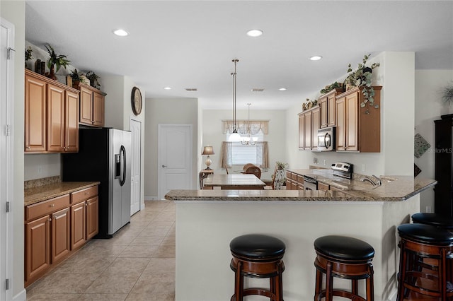 kitchen with hanging light fixtures, light tile patterned floors, kitchen peninsula, stone counters, and stainless steel appliances