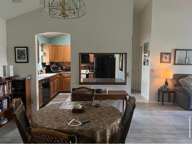 dining space featuring sink, high vaulted ceiling, a chandelier, and light wood-type flooring