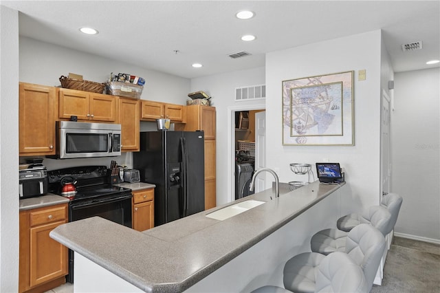 kitchen with sink, washer and dryer, a kitchen breakfast bar, kitchen peninsula, and black appliances