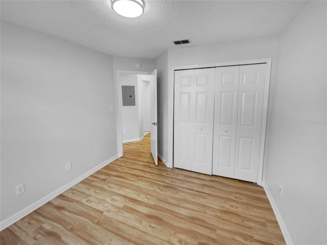 unfurnished bedroom with light hardwood / wood-style floors, a closet, a textured ceiling, and electric panel