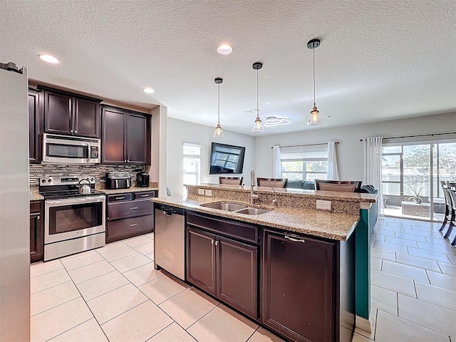 kitchen featuring dark brown cabinetry, sink, hanging light fixtures, appliances with stainless steel finishes, and an island with sink