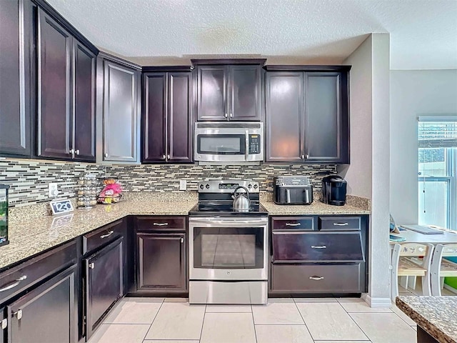 kitchen with dark brown cabinetry, stainless steel appliances, light stone countertops, and backsplash