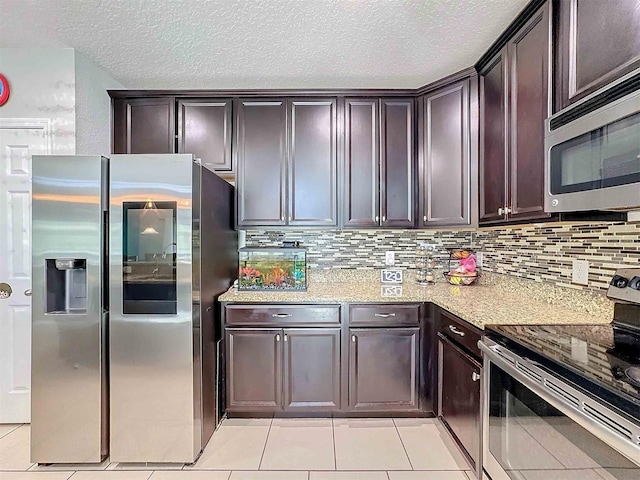 kitchen featuring light stone counters, tasteful backsplash, dark brown cabinets, a textured ceiling, and appliances with stainless steel finishes