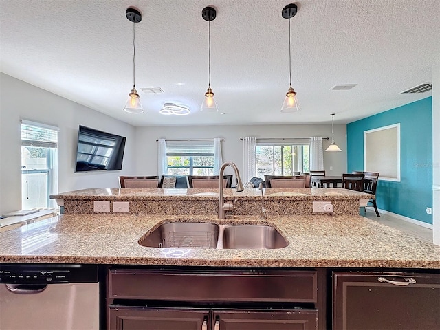 kitchen with pendant lighting, dishwasher, sink, and light stone counters