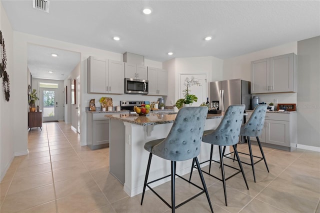 kitchen featuring gray cabinets, dark stone countertops, a breakfast bar area, a kitchen island with sink, and stainless steel appliances