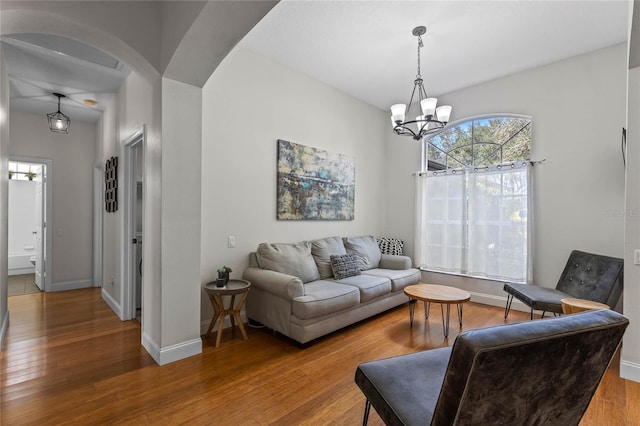 living area featuring arched walkways, wood-type flooring, baseboards, and an inviting chandelier