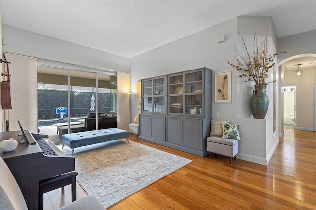 living area featuring arched walkways, a textured ceiling, wood finished floors, and baseboards