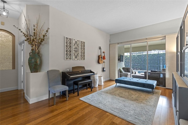 living room with arched walkways, a textured ceiling, wood finished floors, and baseboards