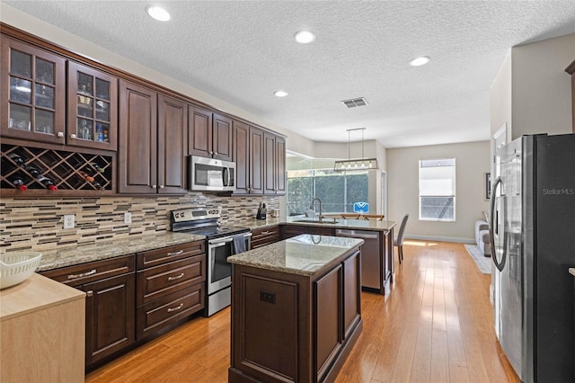 kitchen featuring visible vents, a kitchen island, stainless steel appliances, dark brown cabinets, and light wood-type flooring