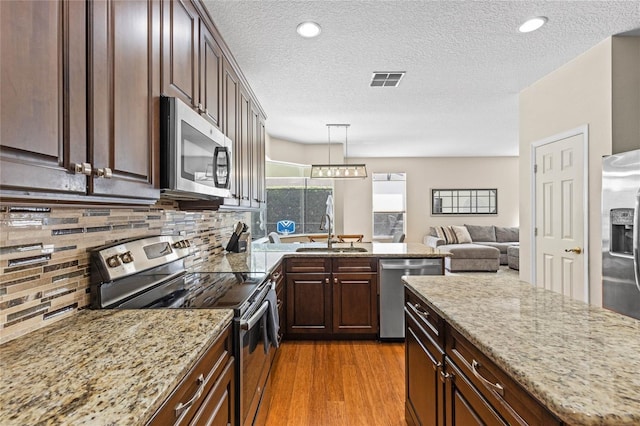 kitchen with dark brown cabinetry, a sink, appliances with stainless steel finishes, decorative backsplash, and light wood finished floors