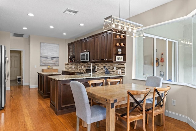 kitchen featuring tasteful backsplash, visible vents, appliances with stainless steel finishes, dark brown cabinets, and light wood-style floors