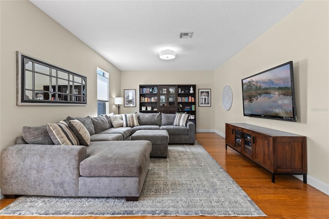 living area featuring visible vents, a textured ceiling, baseboards, and wood finished floors