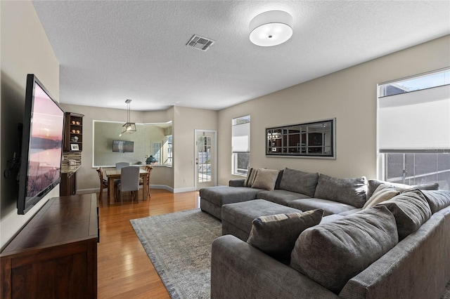 living room with light wood-style floors, visible vents, a textured ceiling, and baseboards