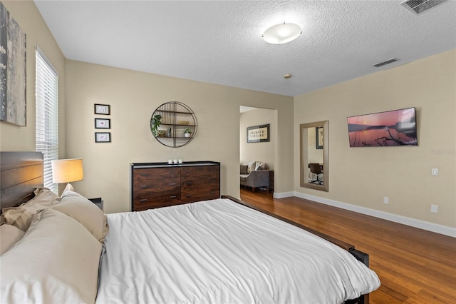 bedroom with a textured ceiling, wood finished floors, visible vents, and baseboards