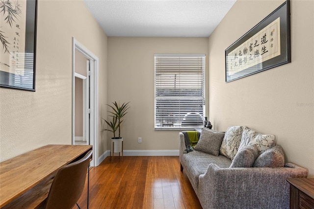 living area with a textured ceiling, wood-type flooring, and baseboards