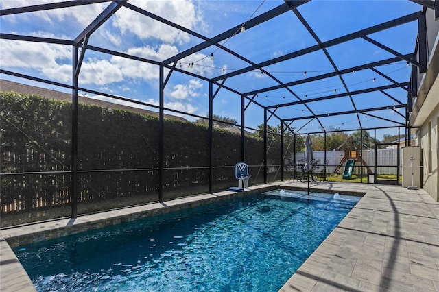 view of pool featuring glass enclosure, a patio, a playground, and a fenced backyard