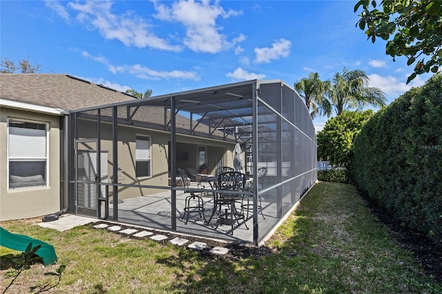 rear view of property with a lawn, roof with shingles, a lanai, a patio area, and stucco siding