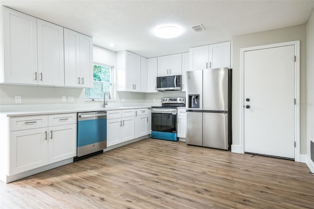 kitchen with appliances with stainless steel finishes, a textured ceiling, white cabinets, and light hardwood / wood-style floors