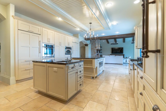 kitchen with cream cabinetry, an island with sink, a sink, and oven