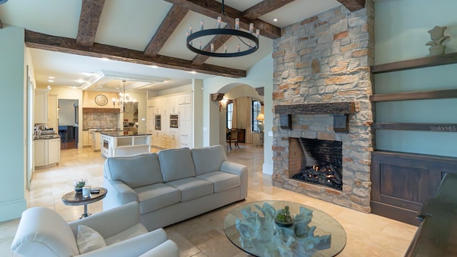 living area with light tile patterned floors, arched walkways, beamed ceiling, an inviting chandelier, and a fireplace