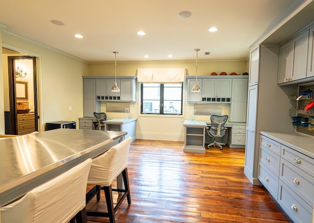 kitchen featuring dark wood-style flooring, built in desk, gray cabinets, stainless steel counters, and ornamental molding