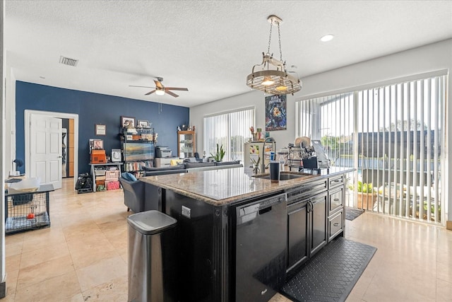 kitchen featuring visible vents, dishwasher, dark cabinets, decorative light fixtures, and a kitchen island with sink