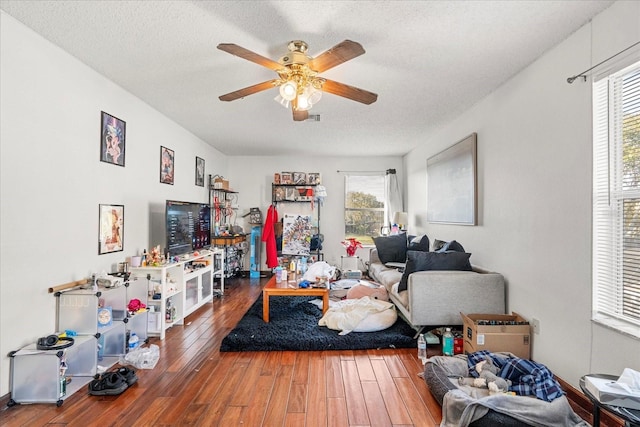 living room featuring visible vents, a textured ceiling, a ceiling fan, and wood finished floors