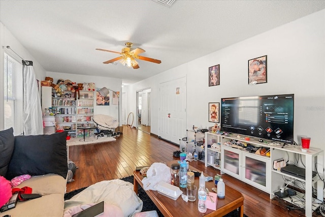 living room featuring dark wood-type flooring, a textured ceiling, and a ceiling fan