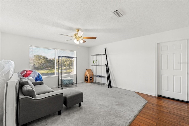 living area featuring a textured ceiling, wood finished floors, a ceiling fan, visible vents, and baseboards