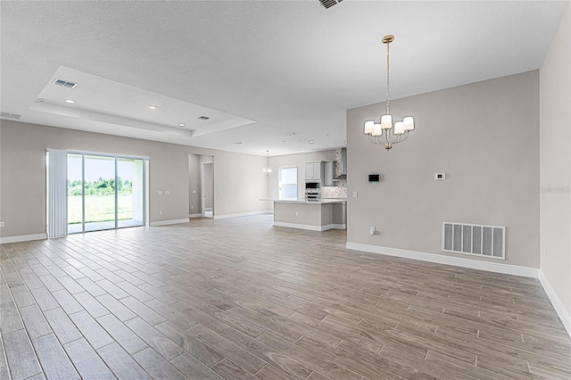 unfurnished living room featuring a raised ceiling, an inviting chandelier, and light hardwood / wood-style floors