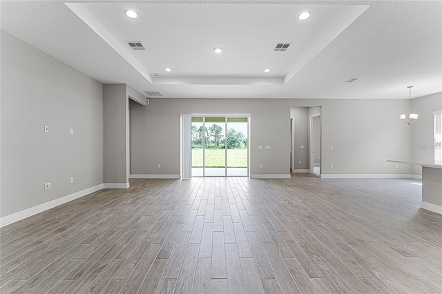 empty room featuring an inviting chandelier, a tray ceiling, light hardwood / wood-style floors, and a textured ceiling