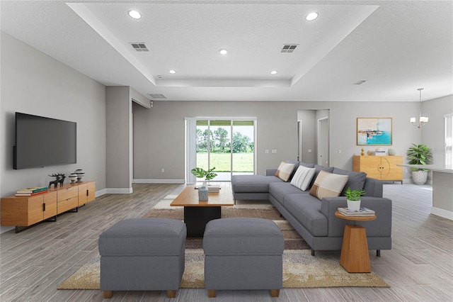 living room featuring an inviting chandelier, a raised ceiling, a textured ceiling, and light wood-type flooring