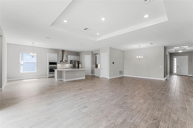 unfurnished living room with a notable chandelier, light hardwood / wood-style floors, and a raised ceiling