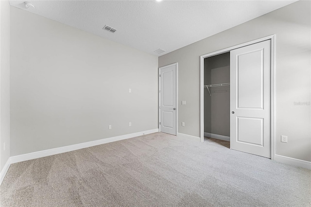 unfurnished bedroom featuring light carpet, a textured ceiling, and a closet