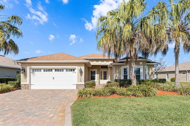 view of front of house featuring a garage, stone siding, decorative driveway, a front lawn, and stucco siding