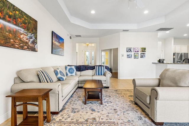 living room with a tray ceiling, light tile patterned flooring, visible vents, and baseboards