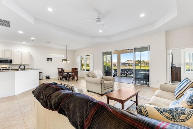living room with a tray ceiling, visible vents, and a healthy amount of sunlight