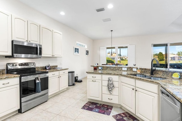 kitchen with light stone counters, a sink, white cabinets, appliances with stainless steel finishes, and pendant lighting