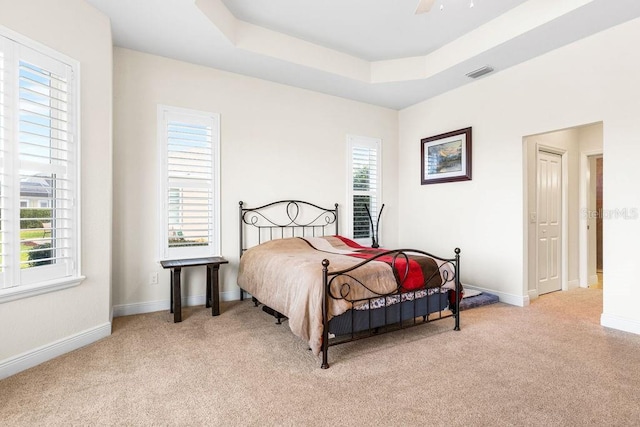 bedroom featuring a tray ceiling, visible vents, light carpet, ceiling fan, and baseboards