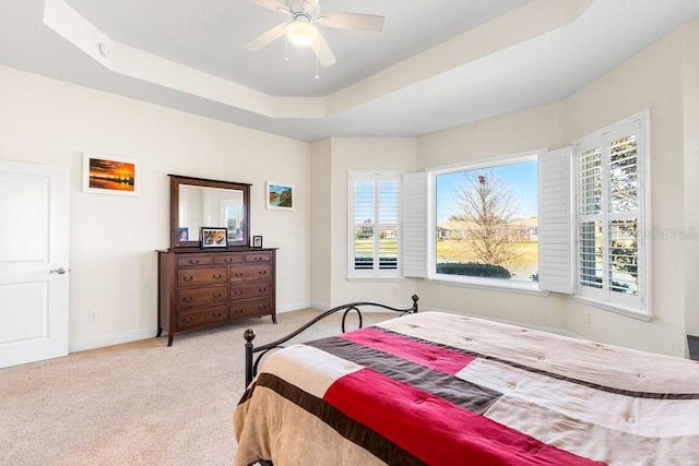 bedroom featuring baseboards, multiple windows, a tray ceiling, and light colored carpet
