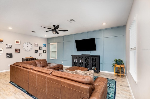 living room featuring visible vents, a decorative wall, light wood-style flooring, and baseboards