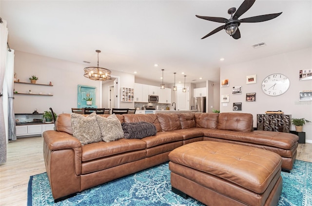 living area with light wood-style floors, recessed lighting, visible vents, and ceiling fan with notable chandelier