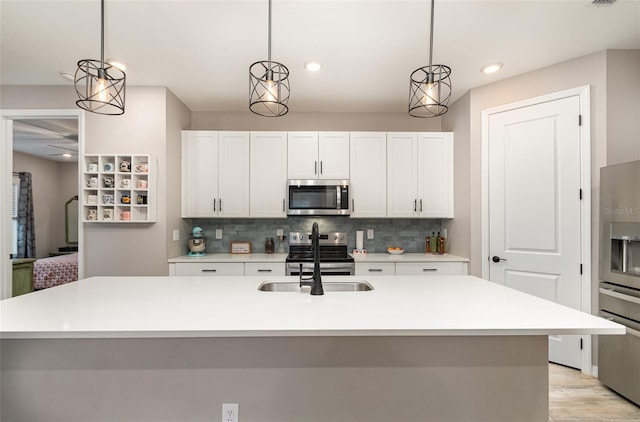 kitchen with an island with sink, appliances with stainless steel finishes, light countertops, and pendant lighting