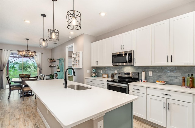 kitchen with a kitchen island with sink, stainless steel appliances, a sink, light countertops, and decorative light fixtures